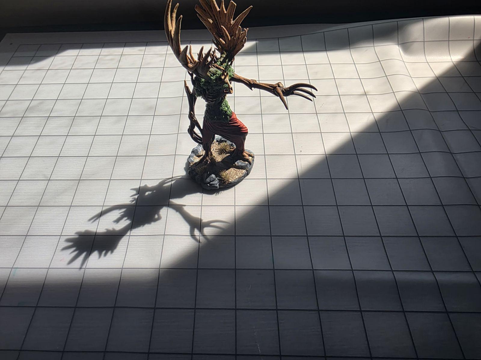 A painted tree-creature miniature standing on the heyTrace grid mat in a beam of sunlight
