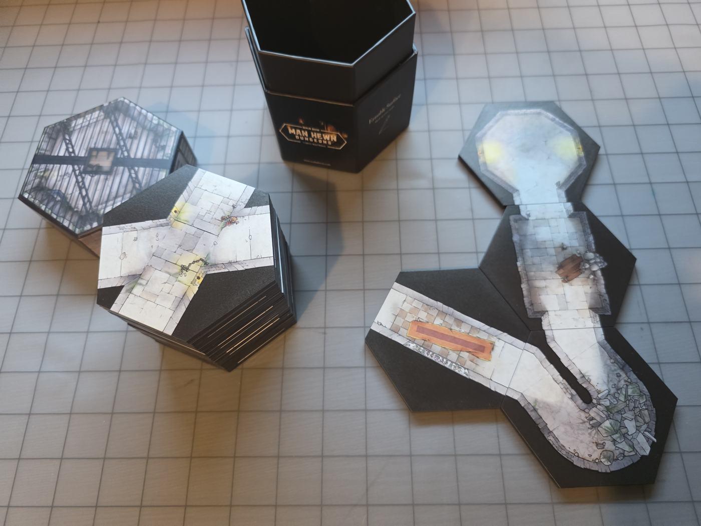 Four Realm Brew hex tiles snapped together into a dungeon path, beside a stack of tiles and the Man Hewn Dungeons box