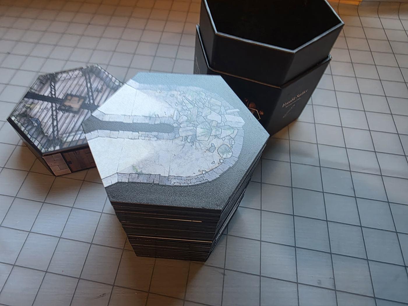 A tall stack of Realm Brew hex tiles next to the open hexagonal box