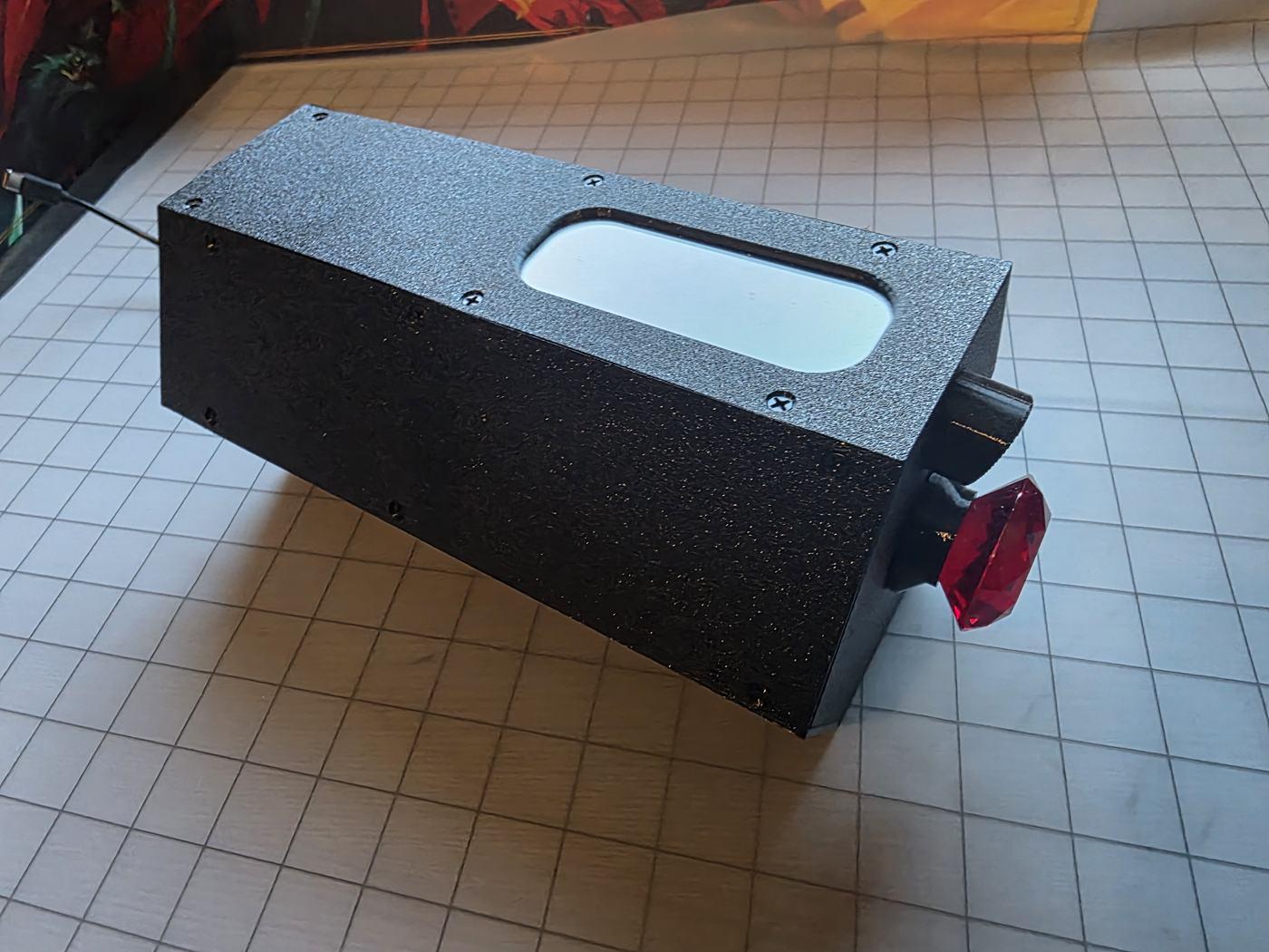 The black ScentedRealms Scent Engine with a red gem knob, on a grid battle mat
