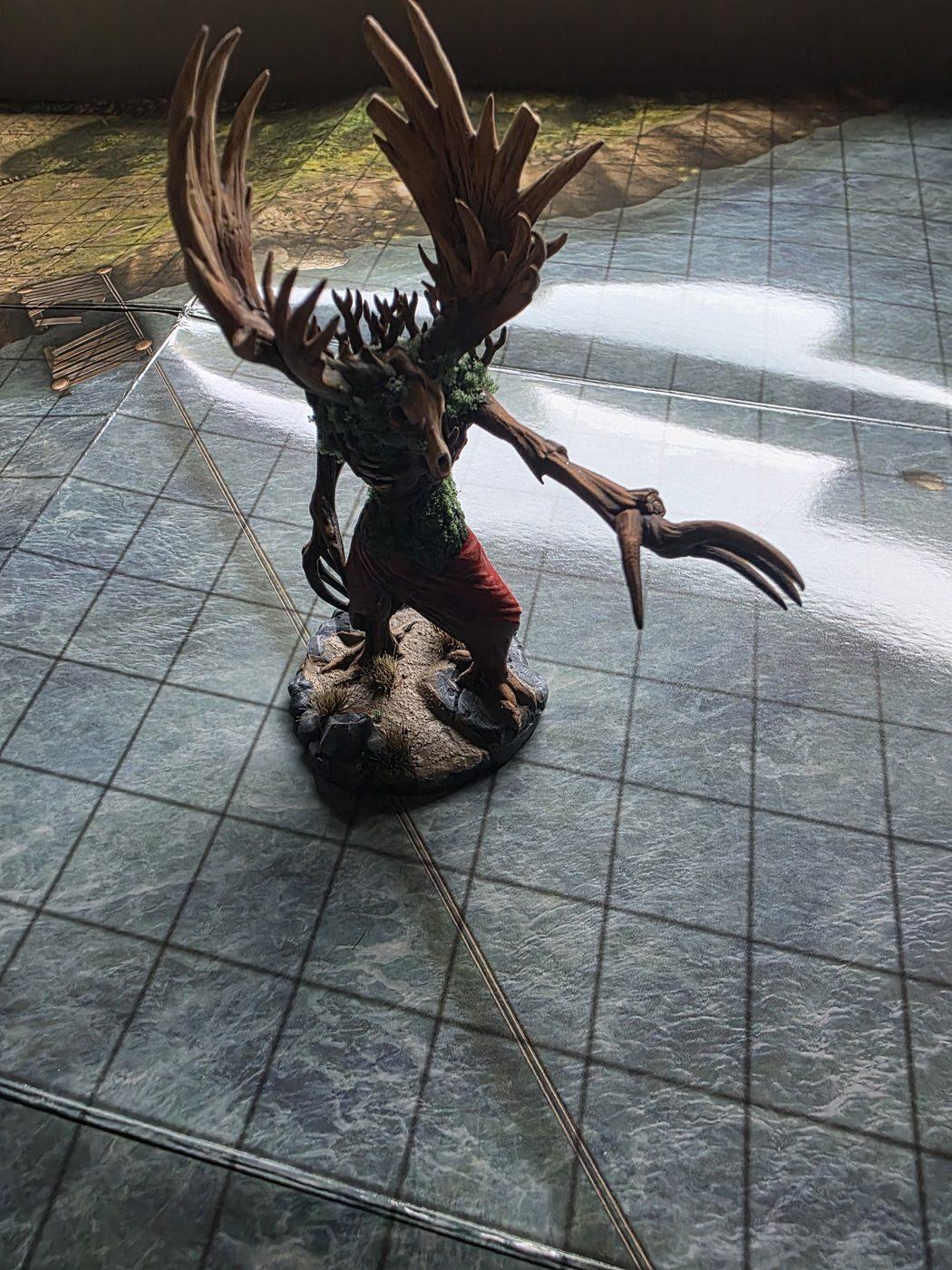 A painted tree-creature miniature standing on the river crossing map, the grid clear across the water